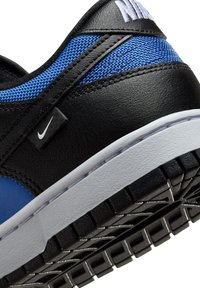 Sneaker in pelle nera con accenti in rete blu, caratterizzato da una suola in gomma bianca e un battistrada testurizzato nero. Include un piccolo etichetta con il logo Nike.