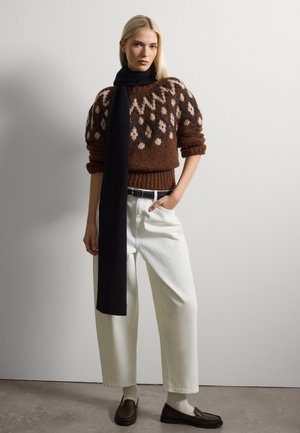 Pull marron à motifs avec des accents crème et noir, pantalons blancs taille haute, écharpe noire et mocassins marron. Texture lisse, coupe décontractée.