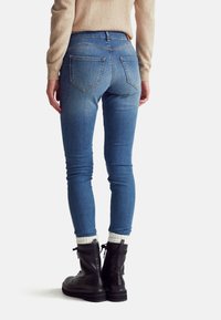 Jeans de denim ajustados en azul claro con una cintura de altura media. Presenta dos bolsillos traseros y un ajuste slim. Se usa con botas negras con cordones y calcetines blancos.