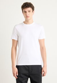 Witte katoenen t-shirt met korte mouwen en een ronde hals, gladde textuur, met een subtiel logo op de borst. Gecombineerd met donkere broeken.