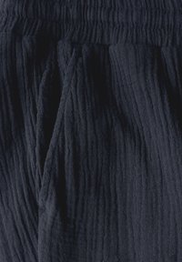 Námořnicky modrá, texturovaná látka se zmačkaným vzorem. Vybavena elastickým pasem a volným střihem, ideální pro pohodlné nošení.