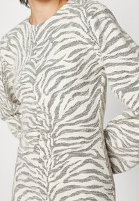 Biały sweter z czarnym wzorem w zebry, wykonany z teksturowanej tkaniny, o dopasowanym kroju i długich rękawach.