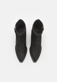 Botine negre din suede până la gleznă, cu vârfuri ascuțite, detaliu cu fermoar și o textură netedă, având un design curbat subtil pe parte superioară.