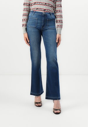 Dark blue flared jeans with a mid-rise waist, five pockets, and contrasting stitching. Paired with black strappy sandals.