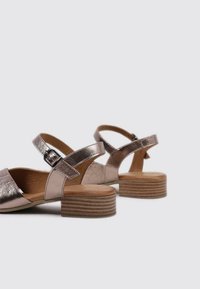 Sandalias metálicas en oro rosa con punta abierta, pequeño tacón cuadrado, correa en el tobillo y detalle de hebilla. Textura suave con tacón de madera.