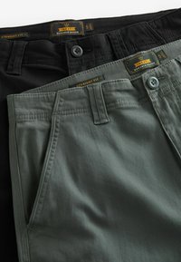 Zwei Paar gerade geschnittene Hosen in Schwarz und Olivgrün. Hergestellt aus strapazierfähigem Stoff mit flachen Fronttaschen und Knopfverschluss.