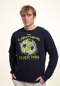 Mörkblå sweatshirt med ett grafiskt tryck av en fotboll omgiven av elektriska bågar och text, tillverkad av bomullsmaterial.