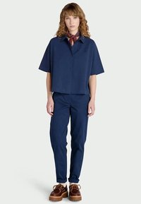 Camisa de manga curta azul-marinho com gola e botões, combinada com calças azuis-marinho a condizer. Tecido leve e texturizado. Acessórios incluem um lenço.