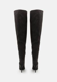 Sorte over-kneet støvler med et strømlinjeformet design, glat tekstur, stiletto hæle og detaljer med lynlås på siden. Ensfarvede uden mønstre.