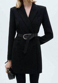 Abito giacca sartoriale nero con maniche lunghe, bottoni doppi, vita con cintura caratterizzata da una fibbia circolare dorata e due tasche laterali.