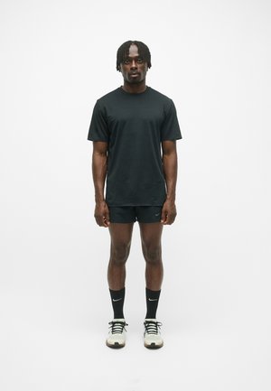 T-shirt noire et shorts, tous deux en tissu lisse. Baskets noires avec des accents blancs, accompagnées de chaussettes noires. Design minimaliste.