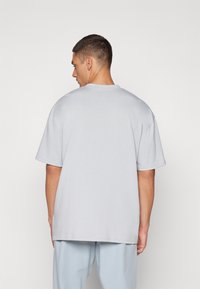 Lys grå oversized t-skjorte laget av mykt materiale, med rund hals og korte ermer, i en avslappet passform uten synlige mønstre.