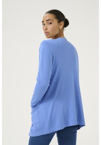 Pull léger à manches longues de couleur bleu clair, avec une coupe décontractée, un détail de poche sur le côté gauche et un motif de tricot texturé.