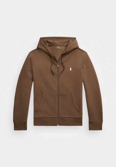 Sweatshirt castanho com fecho éclair e capuz, textura macia, bolsos tipo canguru e um pequeno logótipo branco no peito esquerdo. Design simples e mangas longas.