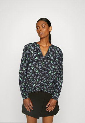 Blusa floral em azul-marinho com padrões em verde e branco, apresentando um decote em V e mangas longas e franzidas. Usada com uma saia preta.