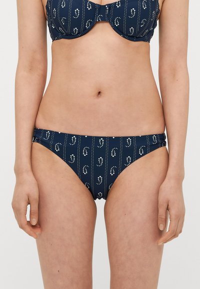 Bas de bikini bleu marine avec un motif. Présente des points blancs et des lignes ; fabriqué en matériau extensible avec des fronces sur les côtés.