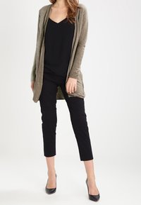 Oliwkowo-zielony kardigan z otwartym przodem, o prążkowanej fakturze, zestawiony z czarnym topem z dekoltem w serek i czarnymi, krótkimi spodniami. Czółenka na obcasie dopełniają stylizację.