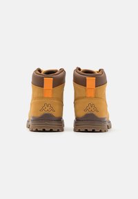 Botas de senderismo marrones y amarillo mostaza con una parte superior texturizada, cuello acolchado y una lengüeta en el talón de color naranja; cuenta con un detalle de logo en la parte trasera.