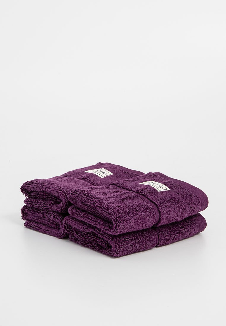 Set van vier diep paarse handdoeken, gemaakt van badstof, netjes gevouwen, met een klein wit label op elke handdoek. Zachte, pluizige textuur.