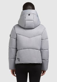 Giacca imbottita grigia con cappuccio, caratterizzata da una texture liscia e cuciture a zig-zag, impreziosita da una patch con logo vicino all'orlo.