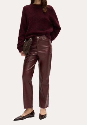 Kvinde iført en bordeauxfarvet, blød striktrøje, højtaljede bordeaux læderbukser, holder en brun clutch og har sorte spidse flade sko med øjer.