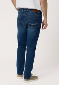 Jeans de mezclilla azul oscuro con un diseño de pierna recta, que cuentan con una parche de cuero marrón y dos bolsillos traseros con costuras en contraste.