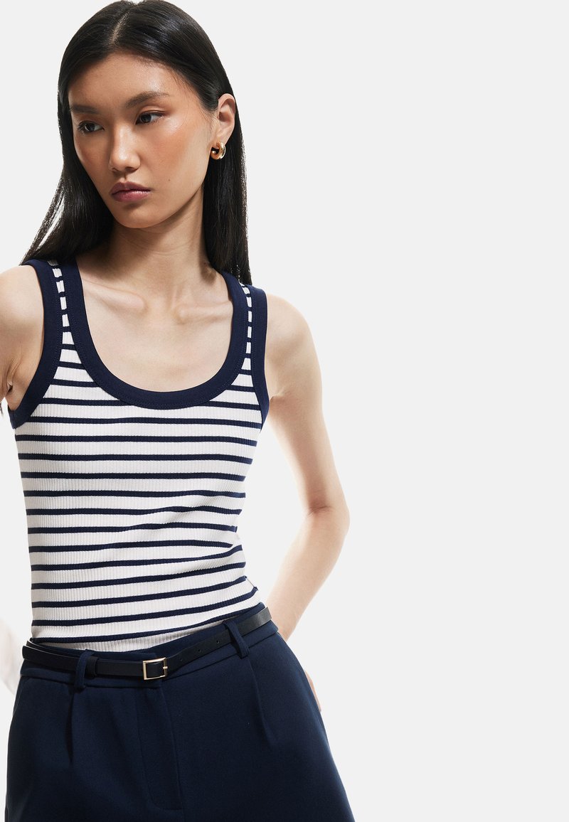 Marineblauwe en witte gestreepte tanktop met een geribbelde textuur, voorzien van een brede ronde hals en bijpassende smalle schouderbandjes, gecombineerd met marineblauwe broeken.