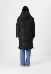 Black puffer coat with a hood, featuring a quilted diamond pattern. The coat is knee-length, paired with light blue wide-leg jeans.