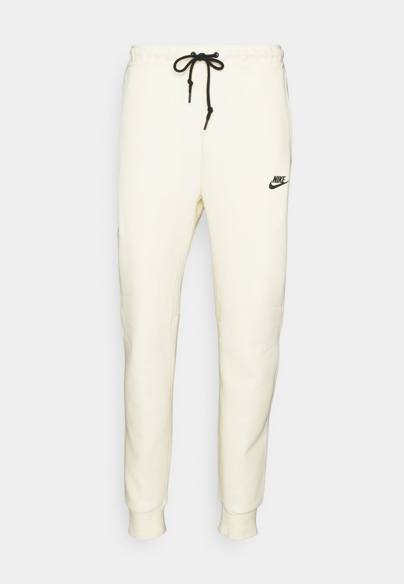 Cremefarbene Nike-Sweatpants mit schwarzem Logo, elastischem Bund und verstellbarem Kordelzug. Sie verfügen über schmal zulaufende Beine und Seitentaschen.