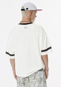 Hvid oversized t-shirt med korte ærmer, mørk kant på kraven og ærmerne samt en lille tekstdetalje på bagsiden.
