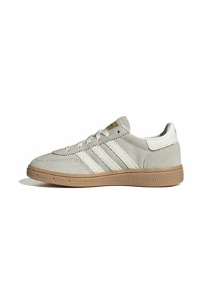 Beiger Wildleder-Sneaker mit weißen Streifen und gummierter, strukturierter Sohle, von der Seite auf weißem Hintergrund gesehen.