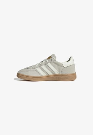Beżowy, niski zamszowy sneaker z białymi paskami i gumową, teksturowaną podeszwą, widziany z boku na białym tle.