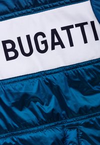Giacca a vento blu con segmento bianco che mostra il logo "BUGATTI". Presenta una texture liscia e lucida e un dettaglio elastico in fondo.