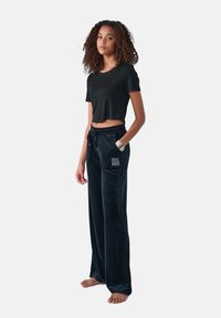 Zwarte cropped t-shirt en donkerblauwe velours broek met elastische tailleband. De broek heeft een "FEEL GOOD" tekstdetail op de linkerzak.