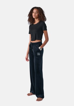 Schwarzes, cropped T-Shirt und dunkelblaue Velourhosen mit elastischem Bund. Die Hose hat ein "FEEL GOOD"-Textdetail auf der linken Tasche.