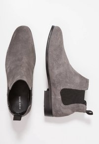 Bottes cheville en daim gris avec un bout arrondi, des panneaux élastiques sur les côtés et un petit talon noir, avec une languette à l'arrière pour faciliter l'enfilage.