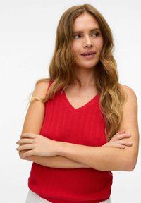 Rød strikket tanktop med v-hals, bølgede kanter og et struktureret mønster. ærmeløs design med en afslappet pasform.