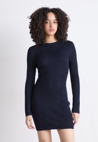 Neulemekko tummansinisestä langasta, jossa on ribbieritys, pitkät hihat ja vartalonmyötäinen siluetti, pyöreä pääntie ja polven ylle ulottuva pituus.