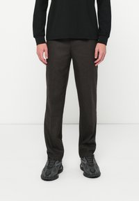 Καφέ μάλλινο παντελόνι με ίσια γραμμή, με λεπτή υφή και καθαρή μέση. Συνδυασμένο με μαύρο μακρυμάνικο τοπ και αθλητικά παπούτσια.