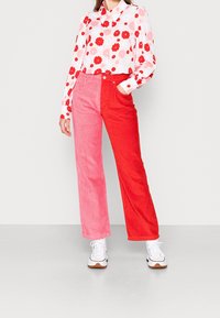 Röda och rosa kordbyxors med vida ben, tillsammans med en vit blus med röda blommönster. Vita sneakers med bruna detaljer.