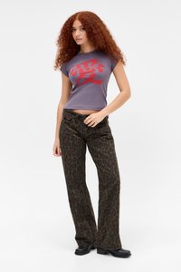 Afgeknotte paarse t-shirt met rode grafische tekst, gecombineerd met bruine broek met luipaardprint en uitlopende pijpen. Model draagt zwarte enkellaarsjes.