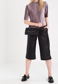Top a maniche corte viola a righe, culotte in finta pelle nera e borsa a tracolla nera con dettagli dorati. Scarpe lucide completano l'outfit.