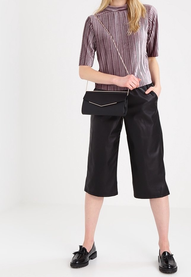 Top a maniche corte viola a righe, culotte in finta pelle nera e borsa a tracolla nera con dettagli dorati. Scarpe lucide completano l'outfit.