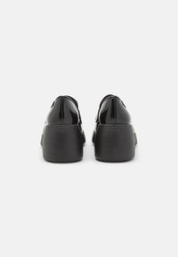 Black patent leather shoes with a rounded shape, low block heel, and textured black rubber outsole. Eyelets are visible at the rear.
