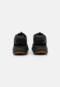 Chaussures de sport noires avec une tige en maille, un col rembourré et une semelle en caoutchouc texturé. Dotées d'une semelle extérieure en caoutchouc qui adhère à la surface et de détails de marque minimalistes.