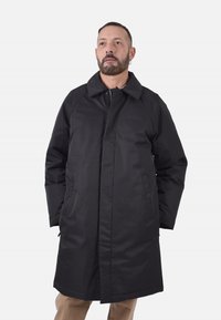 Cappotto lungo nero con colletto strutturato, maniche raglan, due tasche frontali e finitura in tessuto liscia. Caratterizzato da un taglio dritto e chiusura.