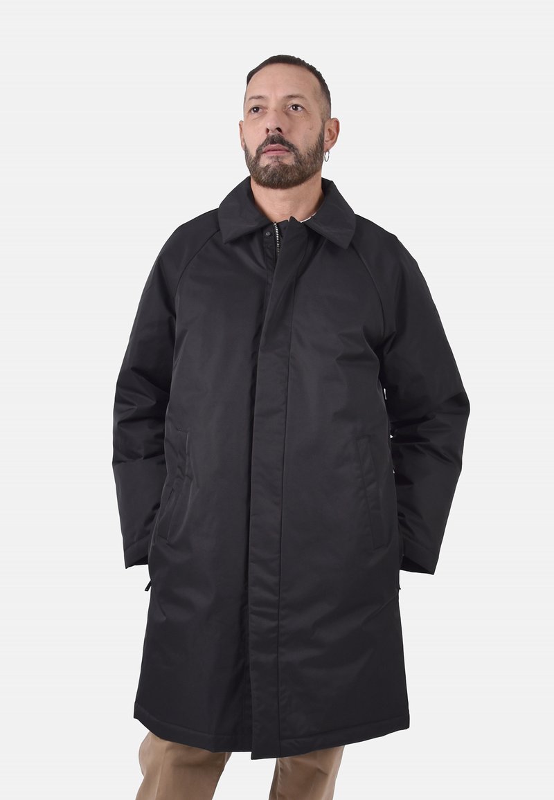 Cappotto lungo nero con colletto strutturato, maniche raglan, due tasche frontali e finitura in tessuto liscia. Caratterizzato da un taglio dritto e chiusura.