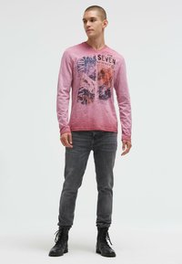 Long-sleeve, light pink t-shirt with graphic print featuring “The Seven Summits.” Paired with gray jeans and black combat boots.