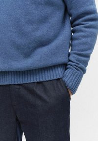 Niebieski sweter z dzianiny z prążkowanymi mankietami i dołem, o teksturowanym wykończeniu. Połączony z ciemnymi, luźnymi spodniami.