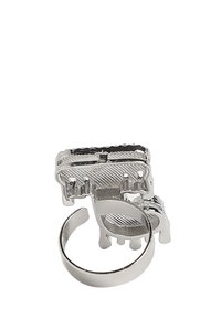 Metalring med en poleret sølvfinish, der har et mekanisk design på toppen og en struktureret bund, åben cirkulær ring for justerbar pasform.